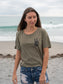 Woman walking on a beach, wearing a green t-shirt with a logo.