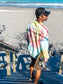 Man walking with a skateboard wearing a tie-dye sweatshirt with a peace symbol on a beach