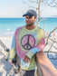 Man walking with a skateboard wearing a tie-dye sweatshirt with a peace symbol on a beach