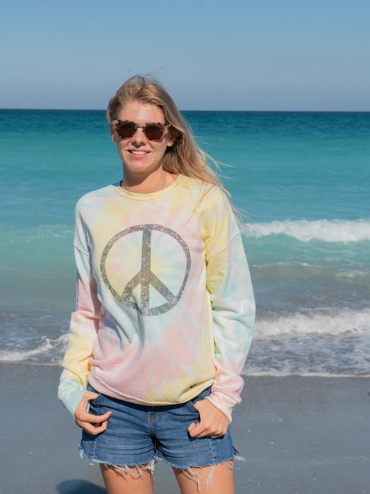 Woman wearing a tie-dye sweatshirt with a peace symbol on a beach