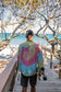 Man walking with a skateboard wearing a tie-dye sweatshirt with a peace symbol on a beach