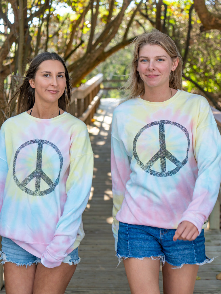 Two women walking with matching tie-dye sweatshirts with a peace symbol on a beach