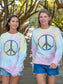 Two women walking with matching tie-dye sweatshirts with a peace symbol on a beach