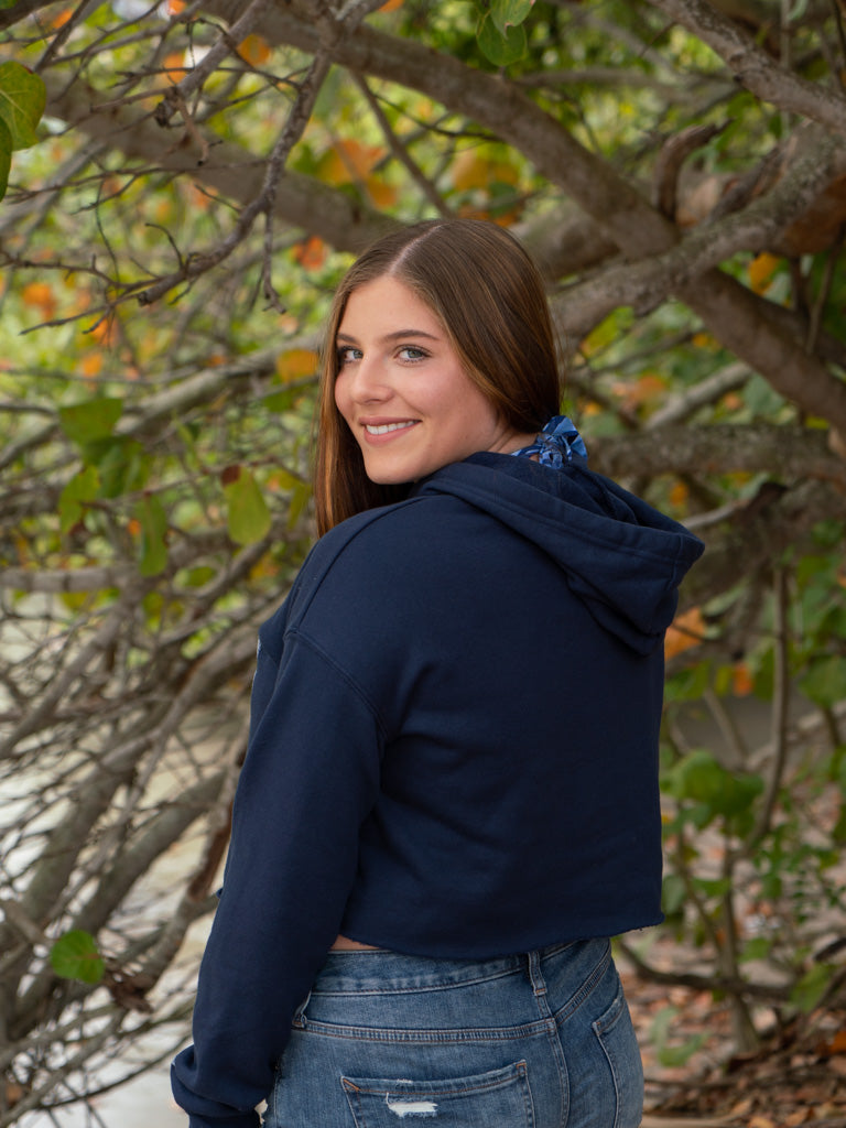 Woman wearing a navy hoodie and denim shorts by a body of water.