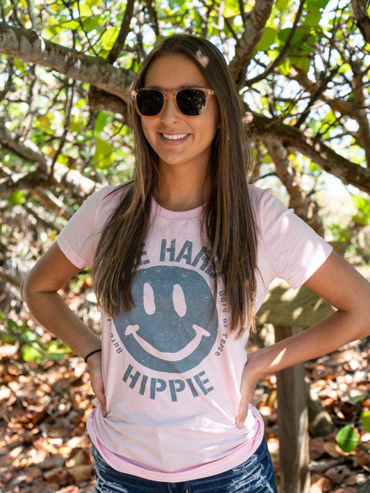 Woman wearing a pink t-shirt with a smiley face design with trees in the background
