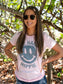 Woman wearing a pink t-shirt with a smiley face design with trees in the background