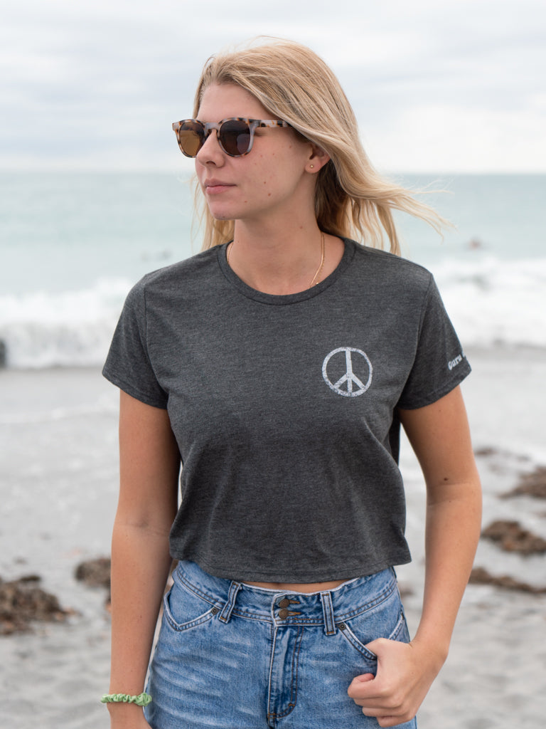 Woman wearing a dark gray t-shirt with a peace symbol on a beach