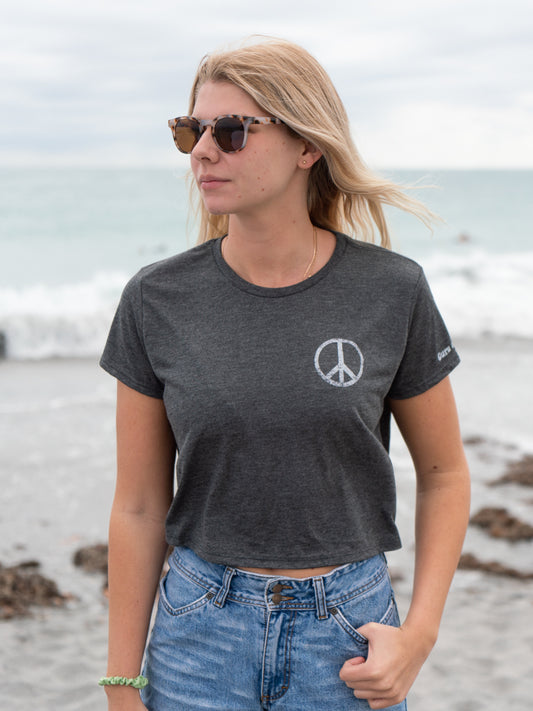 Woman wearing a dark gray t-shirt with a peace symbol on a beach