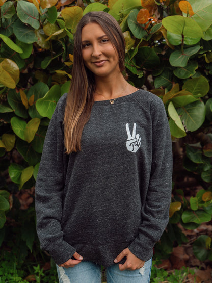 Woman wearing a dark gray sweatshirt with a peace sign design, standing in front of green foliage.