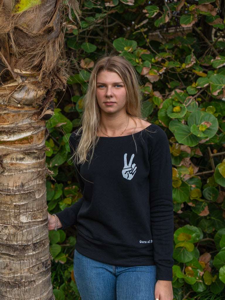 Woman wearing a black sweatshirt with a peace sign design, standing in front of green foliage.
