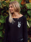 Woman wearing a black sweatshirt with a peace sign design, standing in front of green foliage.