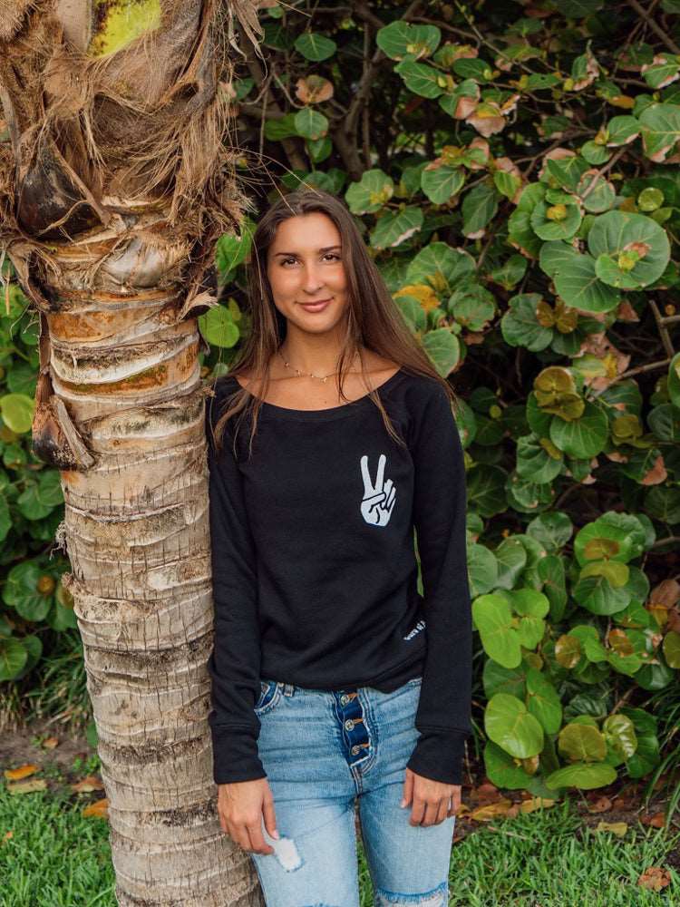 Woman wearing a black sweatshirt with a peace sign design, standing in front of green foliage.