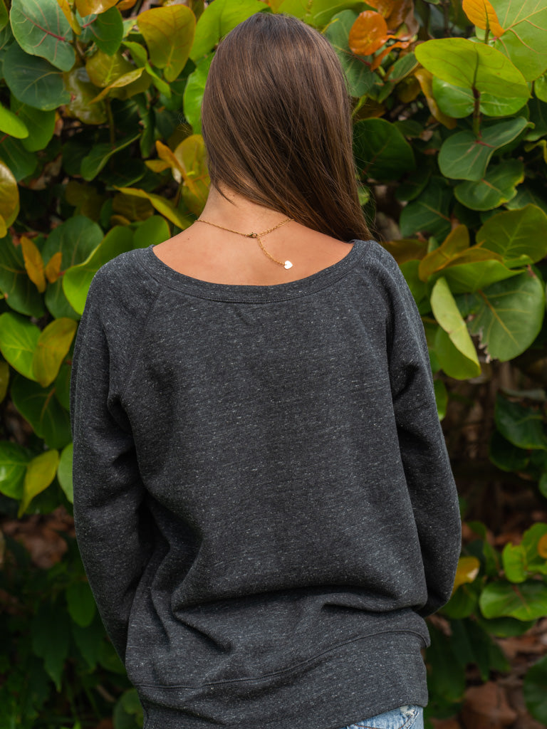Woman wearing a dark gray sweatshirt, standing in front of green foliage.