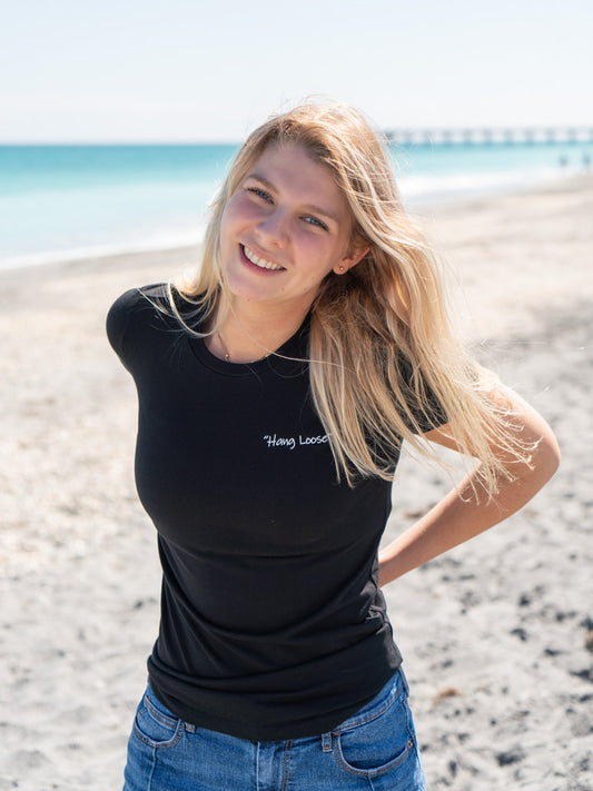 Woman wearing a black t-shirt with a logo, standing outdoors on a beach.