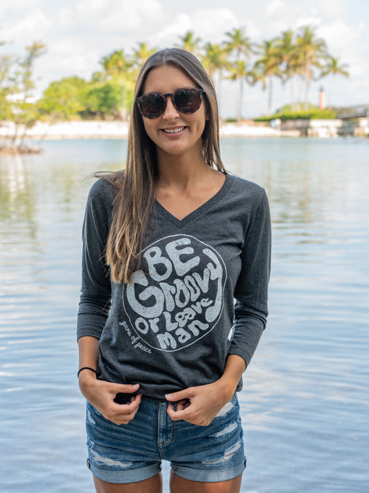 Woman wearing a gray long-sleeve shirt with a graphic design by a body of water.