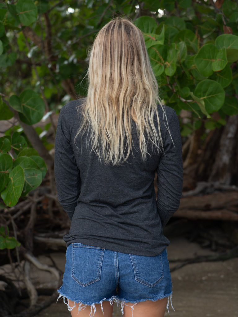 Woman wearing a gray long-sleeve shirt on a beach with leafy background