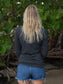 Woman wearing a gray long-sleeve shirt on a beach with leafy background