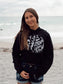 Woman wearing a black hoodie with white text on a beach
