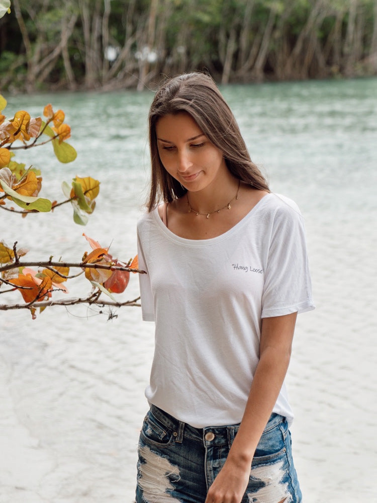 Woman in a white t-shirt and denim shorts standing by a body of water with trees in the background.