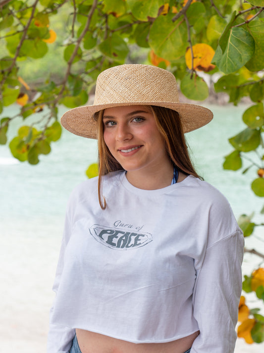 Woman wearing a white long-sleeve crop top with a logo and text, standing under a tree with green leaves.