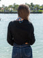 Woman wearing a black long-sleeve crop top, standing by a body of water
