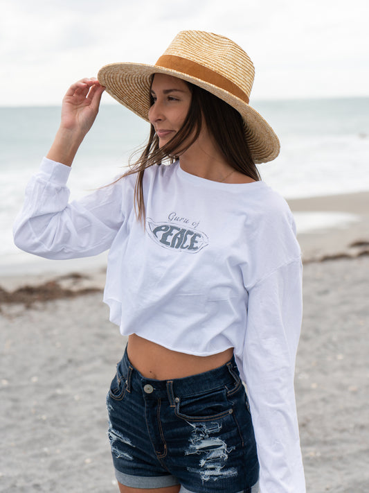 Woman wearing a white long-sleeve crop top with a logo and text, standing on a beach