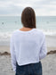 Woman wearing a white long-sleeve crop top with a logo and text, standing on a beach