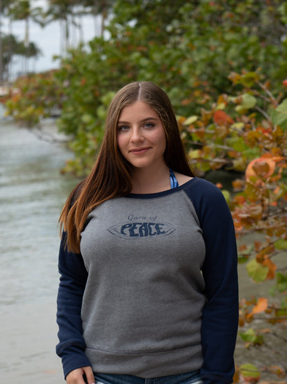 Woman wearing a gray and navy sweatshirt with 'Guru of Peace' text, standing outdoors by water.