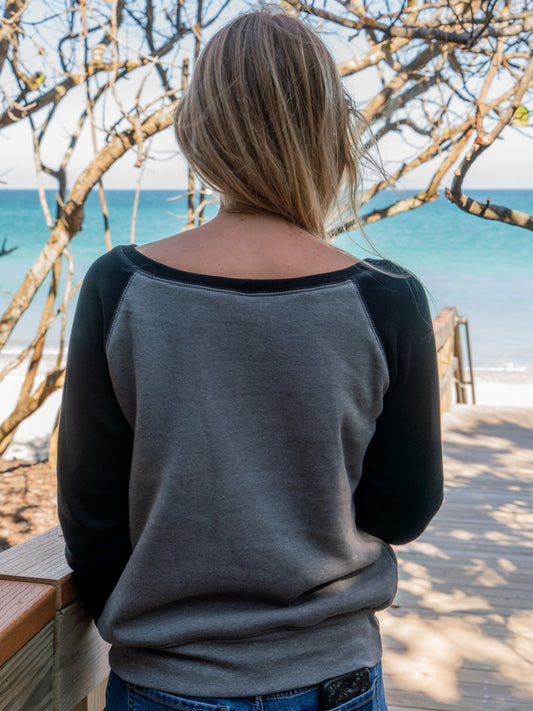 Woman leaning on a wooden railing wearing a crewneck, surrounded by trees