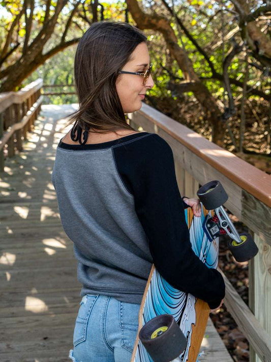 Woman standing by a wooden railing with a skateboard, surrounded by trees