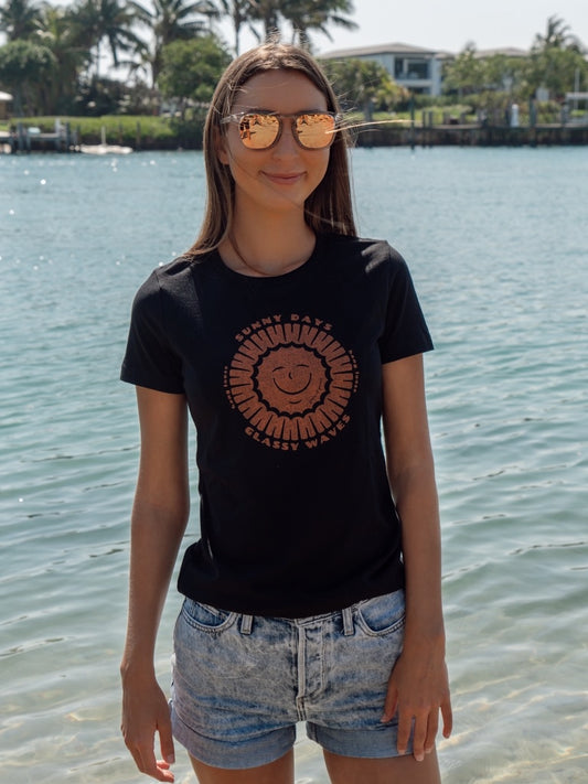 Person wearing a black t-shirt with a smiley face design by the water