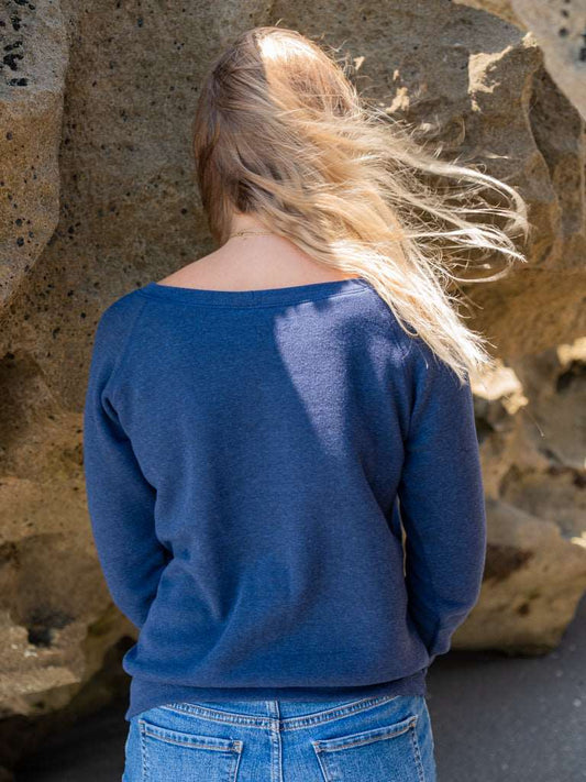 Woman wearing a navy blue sweatshirt, standing against a rocky background.