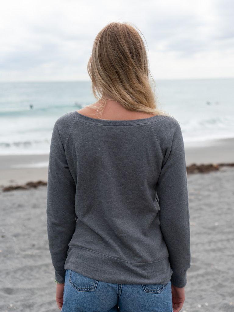 Woman wearing a gray crewneck on a beach with an ocean background