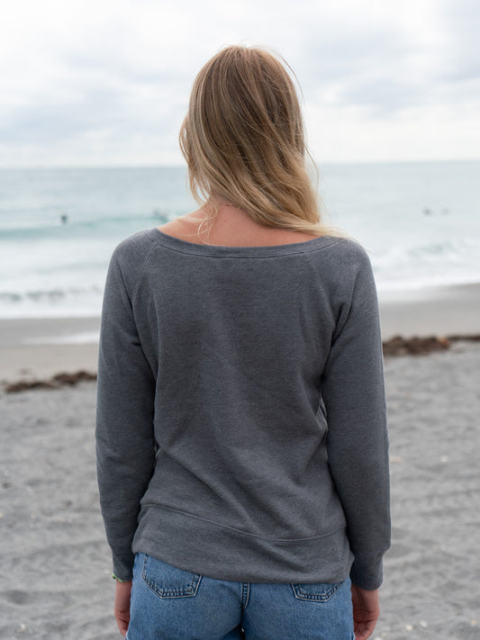 Woman wearing a gray crewneck on a beach with an ocean background