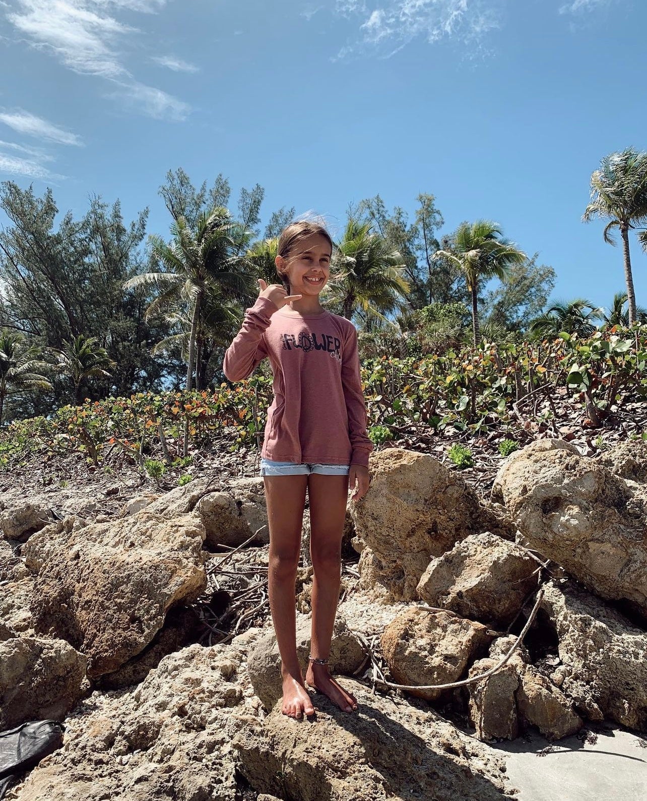 Person standing on rocks with palm trees and blue sky in the background