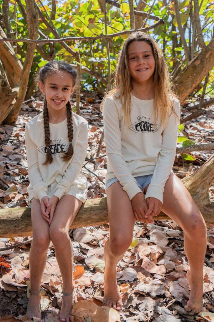 Two young girls wearing a long sleeve shirt with the words 'Guru of Peace' sitting on a log in a forest setting