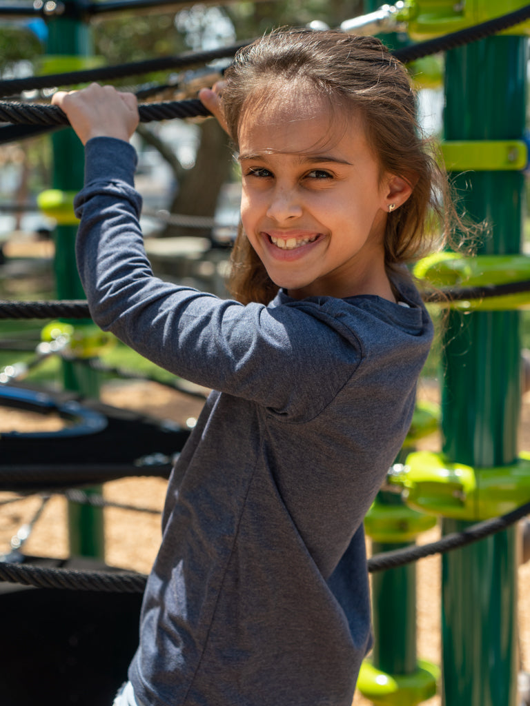 Young girl wearing a grey long sleeve shirt  playing on a playground