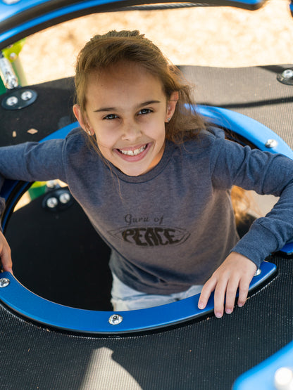 Young girl wearing a grey long sleeve shirt with the words 'Guru of Peace' playing on a playground