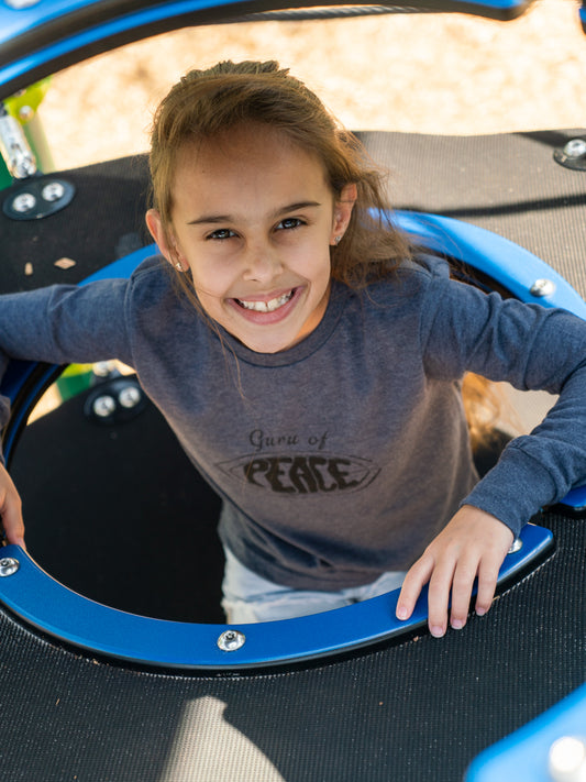Young girl wearing a grey long sleeve shirt with the words 'Guru of Peace' playing on a playground