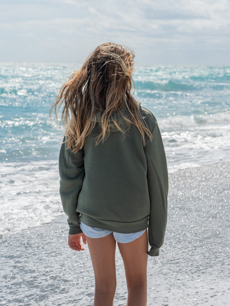 Young girl wearing green hoodie, standing on a beach