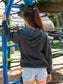 Two young girls wearing grey hoodie with a sun design at a playground