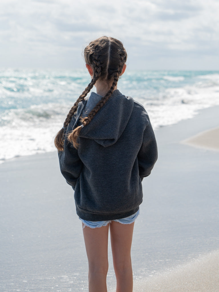 Young girl wearing grey hoodie standing on a beach