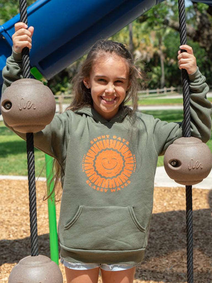 Young girl wearing green hoodie with a sun design, standing in a playground setting