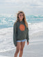 Young girl wearing green hoodie with a sun design, standing on a beach