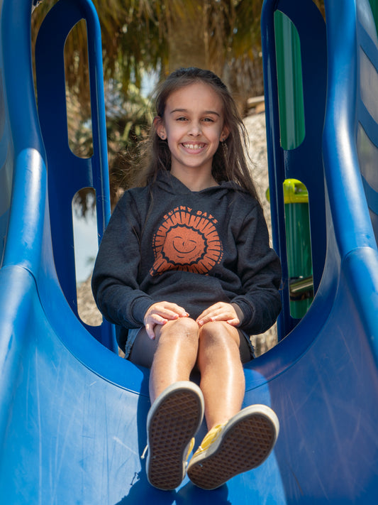 Young girl wearing black hoodies with a sun design, sitting on a slide