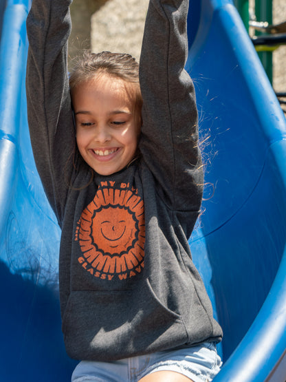Young girl wearing grey hoodies with a sun design, sliding down a slide