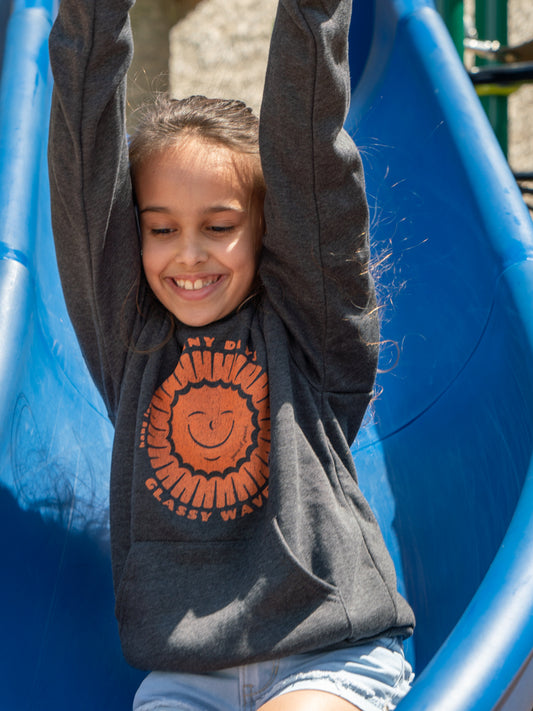 Young girl wearing grey hoodies with a sun design, sliding down a slide