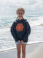 Young girl wearing grey hoodie with a sun design, standing on a beach