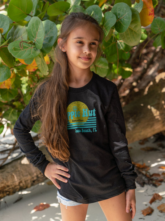 Young girl wearing a black long-sleeve shirt with a graphic design, standing on a beach.