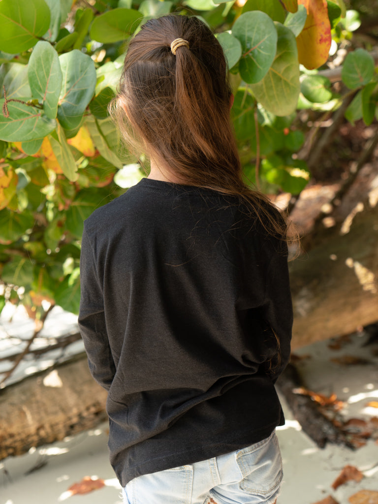 Young girl wearing a black long-sleeve shirt, standing on a beach.